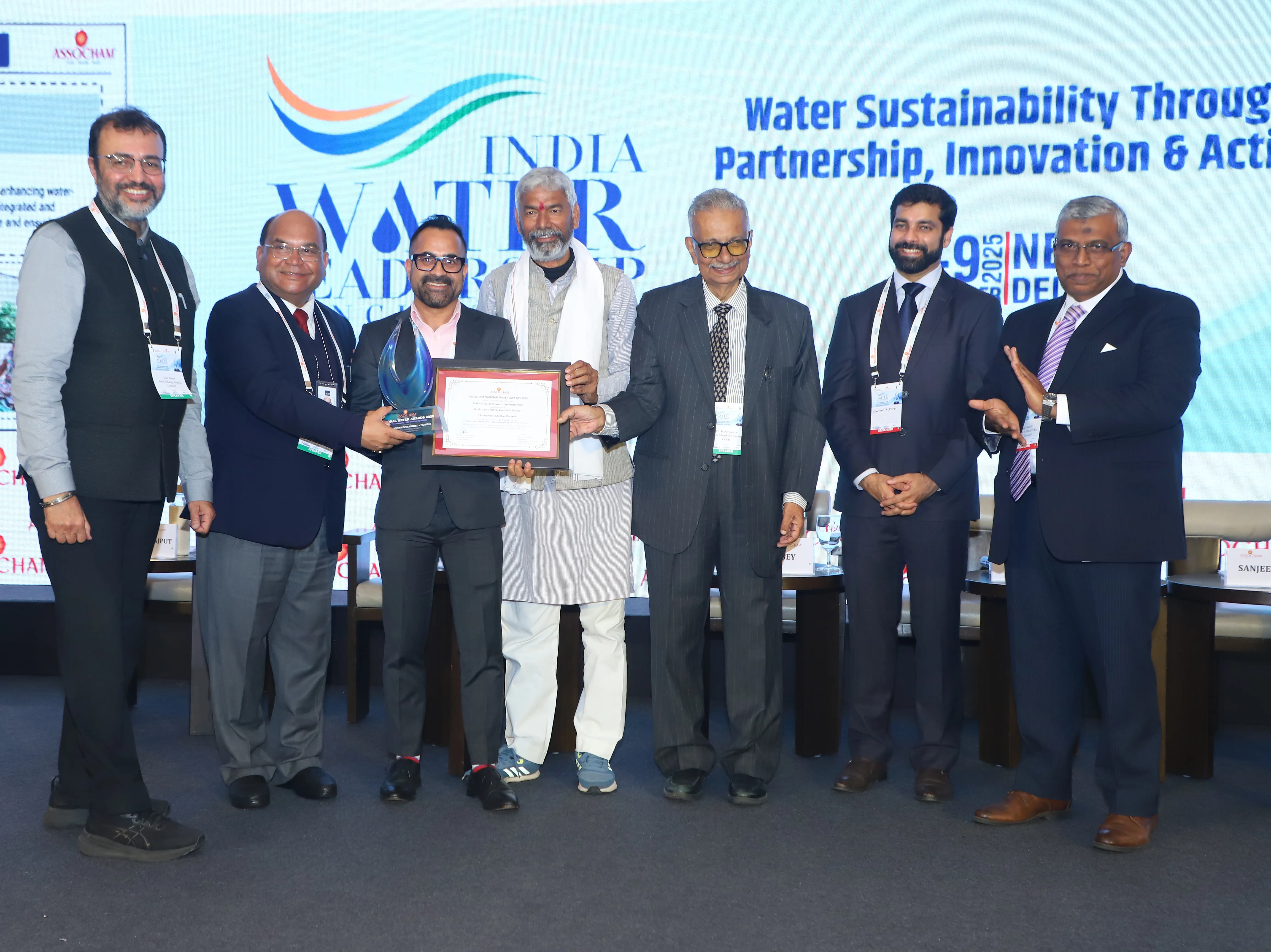 Group of people holding the ASSOCHAM award certificate on stage.