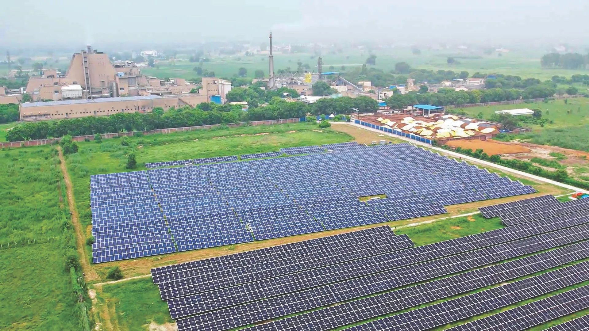 Aerial view of a factory facility next to a large field of solar panels