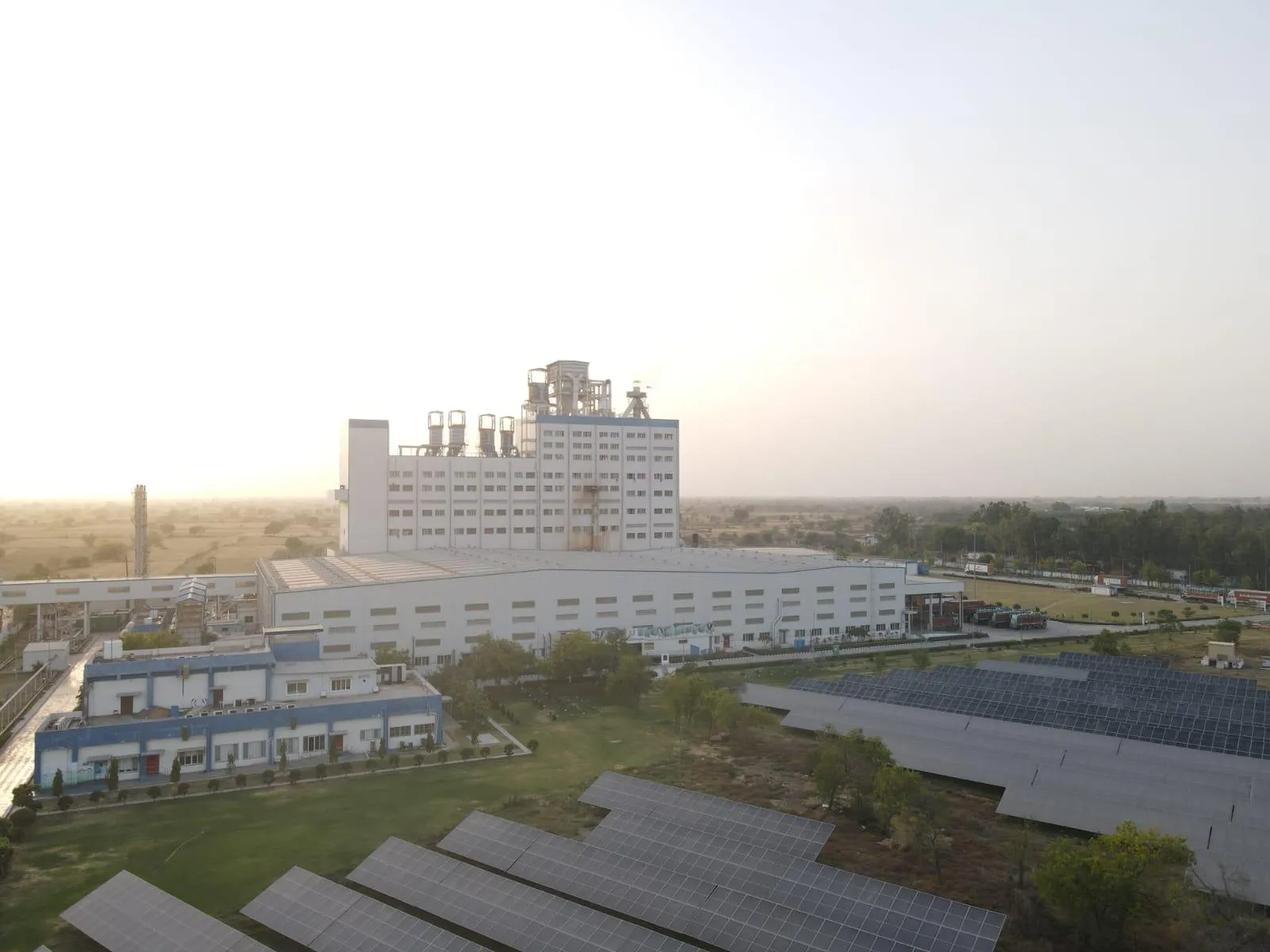 Aerial view of a large manufacturing facility featuring a ground-level solar panel installation at sunrise.